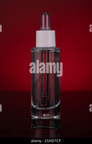 Bouteille compte-gouttes en verre transparent avec liquide sur fond rouge Banque D'Images