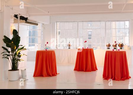 Espace intérieur lumineux avec des tables oranges préparées pour un événement élégant, avec des rafraîchissements en arrière-plan. Banque D'Images