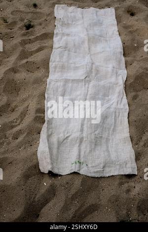 Longue serviette de chanvre sur le sable. La longue toile de chanvre est étalée sur le sable. Le mot chanvre est brodé de fils verts. Banque D'Images