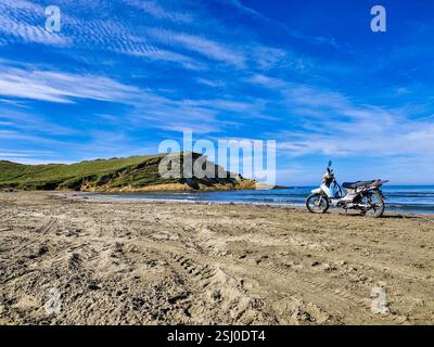 Une moto debout seul sur le rivage de la mer sur la plage de Zvernec en Albanie, au premier plan sont des traces de pneus dans le sable Banque D'Images