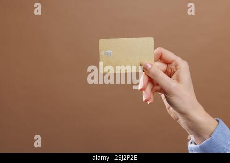 femme tenant la carte de crédit bancaire en or avec paiement sans contact sur fond beige, Banque D'Images