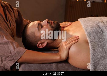 Homme profitant d'un massage apaisant des épaules et du cou dans un spa tranquille, entouré d'un éclairage doux et d'une ambiance relaxante. Banque D'Images