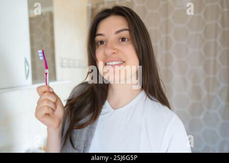 Femme heureuse tient une brosse à dents et sourit, montrant son sourire éclatant. Un brossage régulier empêche l'accumulation de tartre et maintient la santé bucco-dentaire. Banque D'Images