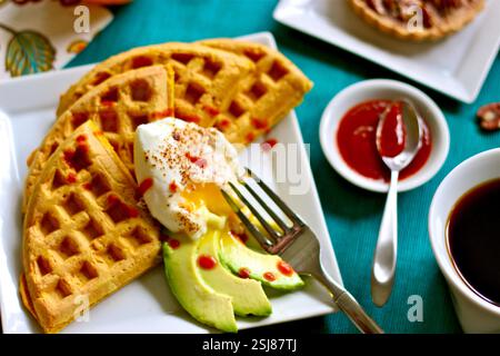 Assiette de brunch salée avec gaufres, œuf poché, avocat tranché et sauce piquante servie avec du café sur fond turquoise éclatant Banque D'Images