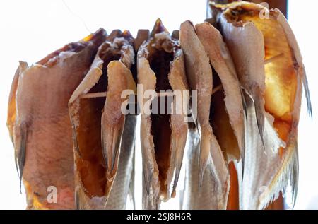 Les poissons séchés sont suspendus sur un support en bois, mettant en valeur leurs surfaces brunes dorées. Le marché côtier est lumineux avec la lumière du jour, mettant en évidence le tradit Banque D'Images