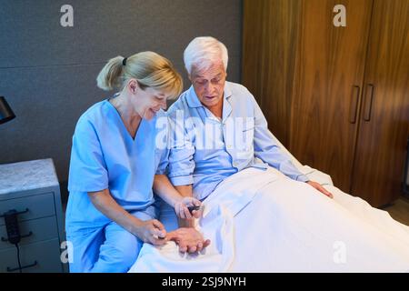 Une infirmière fournit de l'aide à un homme âgé dans un cadre de réadaptation pour les soins de santé et le rétablissement. Banque D'Images
