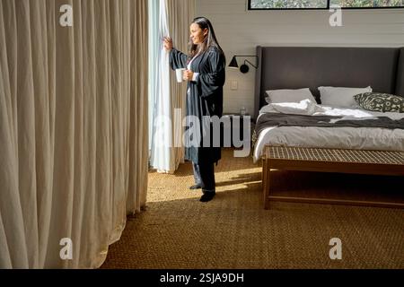 Femme regardant par la fenêtre dans la chambre Banque D'Images