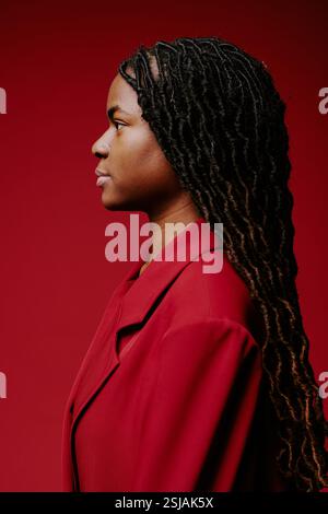 Axé sur le profil latéral des femmes avec de longs cheveux tressés et portant un manteau rouge devant un fond rouge assorti Banque D'Images