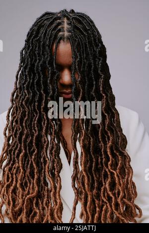 Jeune femme noire avec de longues serrures bouclées souriantes tout en regardant vers le bas, mettant en valeur de beaux cheveux naturels avec des motifs et des textures complexes Banque D'Images