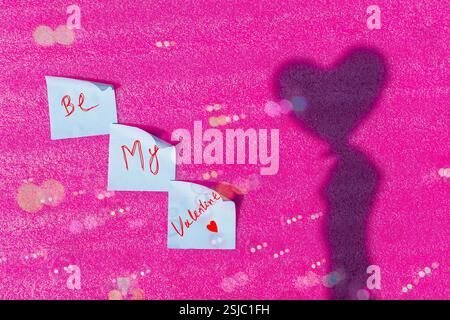Une note autocollante rose avec « Be My Valentine » écrit à la main élégante, sur fond rose doux. Banque D'Images
