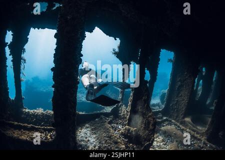 FreeDiver explore les épaves sous-marines, entourées de rayons lumineux et de croissance marine. Plongée libre à l'épave du navire Banque D'Images