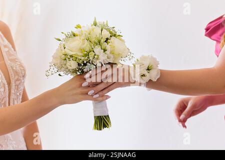 Gros plan d'une demoiselle d'honneur passant un bouquet floral blanc à la mariée. L'accent est mis sur leurs mains et les fleurs de mariage élégantes. Banque D'Images