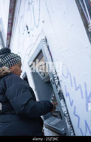 Une femme afro-caribéenne debout à un mur cashpoint dans le sud de Londres, Angleterre, Royaume-Uni. Banque D'Images