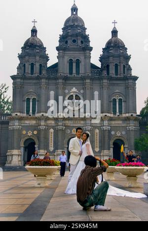 Pékin, CHINE- jeune couple chinois nouvellement marié posant pour un photographe devant l'église catholique sur la rue Wangfujing. Taux de mariage en Chine Banque D'Images