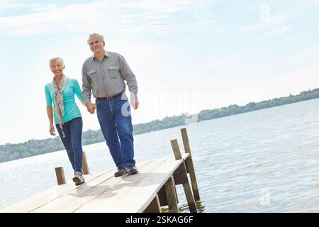 Heureux, âgé et couple marchant sur la jetée pour la retraite, voyage de vacances et destination de voyage. Ci-dessous, les personnes âgées et se tenant la main pour le mariage Banque D'Images