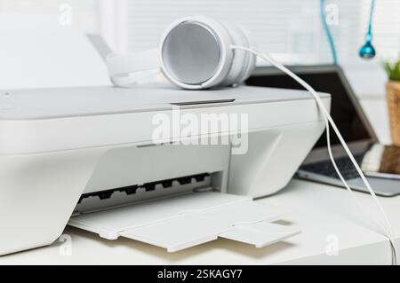 Configuration de bureau moderne avec une imprimante, des écouteurs et un ordinateur portable sur un bureau bien rangé pendant la journée Banque D'Images