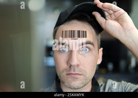 Un homme avec une expression stupide regarde son code qr sur sa tête. Le concept de chipping de la population. Jeune homme avec un code qr sur son front. glo Banque D'Images