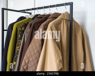 Une rangée de manteaux d'automne et de printemps dans des tons terreux accrochés sur un porte-vêtements élégant. Banque D'Images