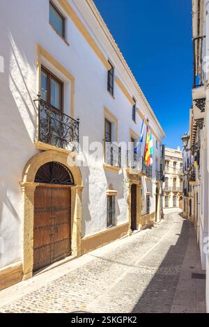 Ville de Ronda en Espagne. Rue pavée baignée de soleil dans une ville historique, avec des bâtiments blanchis à la chaux avec balcons ornés et portes en bois. Banque D'Images