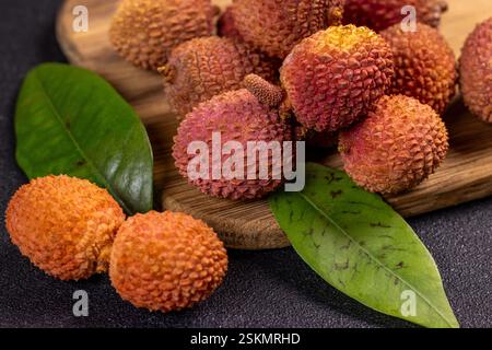 Des litchis mûrs et des feuilles vertes sont disposés sur une planche à découper en bois, mettant en valeur la couleur et la texture vibrantes du fruit Banque D'Images