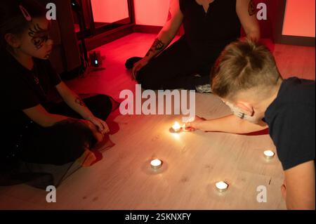 Trois individus, deux enfants et un adulte, participent à un arrangement rituel de bougies sur un plancher en bois. La pièce est faiblement éclairée, coulant un Banque D'Images