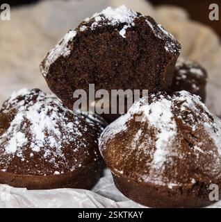 Gros plan d'un muffin au chocolat mordu avec du sucre en poudre sur le dessus, placé sur du papier parchemin. Banque D'Images