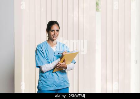 Physiothérapeute écrivant des notes sur le presse-papiers pendant le suivi téléphonique Banque D'Images