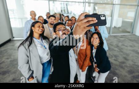 Groupe multiethnique de collègues souriants prenant un selfie ensemble dans un environnement de bureau, soulignant le travail d'équipe, la camaraderie et un plan de travail positif Banque D'Images