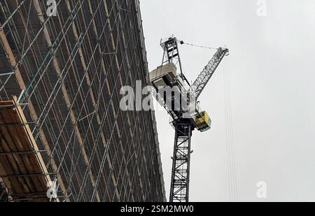 Chantier de construction comprenant une grue imposante, des matériaux de levage, à côté d'un grand bâtiment recouvert d'échafaudages. Banque D'Images