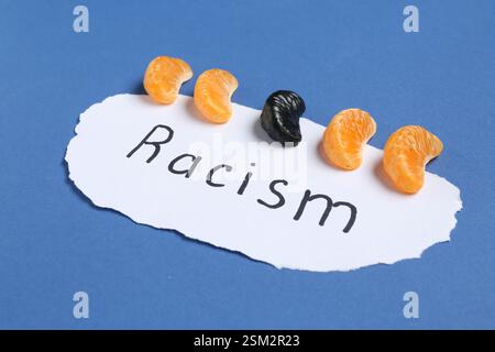 Carte avec mot racisme et segments de mandarine de différentes couleurs sur fond bleu Banque D'Images
