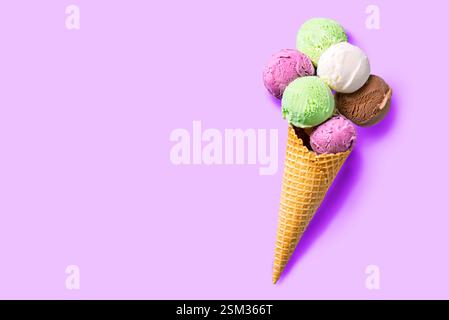 Cône de crème glacée avec diverses cuillères sur fond pastel violet, pose plate créative, espace de copie. Beaucoup de cuillères à crème glacée colorées biologiques dans un cône de gaufre. Banque D'Images
