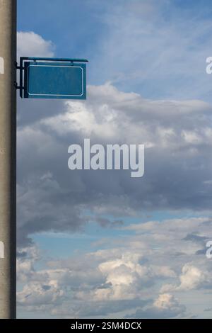 Panneau en métal rectangulaire bleu avec bordure décorative monté sur un poteau, placé sur un fond avec des nuages blancs moelleux et un ciel bleu vif, ev Banque D'Images