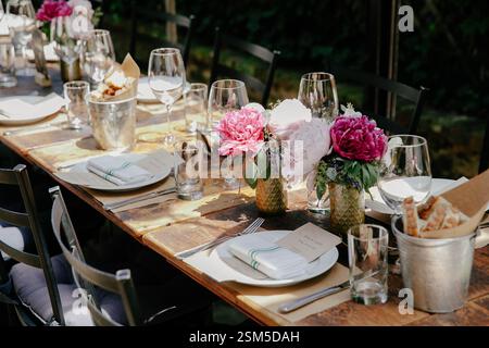 Une superbe table à manger avec des centres de table fleuris et de la verrerie en cristal dans un cadre paisible de jardin. Banque D'Images