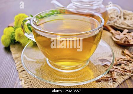 Tisane dans une tasse en verre, une théière sur une serviette de toile de jute, cuillère avec des racines sèches de Rhodiola rosea, fleurs fraîches de Rhodiola rosea sur le fond o Banque D'Images
