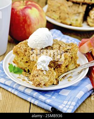 Morceau de gâteau sucré avec de la rhubarbe, des pommes et une boule de glace, menthe, serviette de table, fourchette, tasse sur l'arrière-plan de planches en bois Banque D'Images