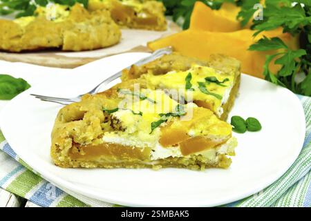 Deux morceau du pâté en croûte de potiron, salé le fromage feta, les oeufs, la crème et les herbes dans un plat sur une serviette, le basilic sur l'arrière-plan des panneaux en bois Banque D'Images