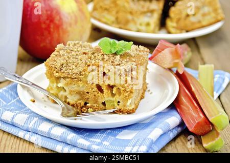 Un morceau de gâteau sucré à la rhubarbe et les pommes, menthe, bleu, serviette tasse sur l'arrière-plan de planches en bois Banque D'Images