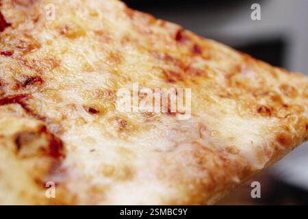 Gros plan d'une tranche de pizza au fromage avec une croûte brune dorée Banque D'Images