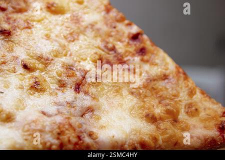 Gros plan d'une tranche de pizza au fromage avec une croûte brune dorée Banque D'Images