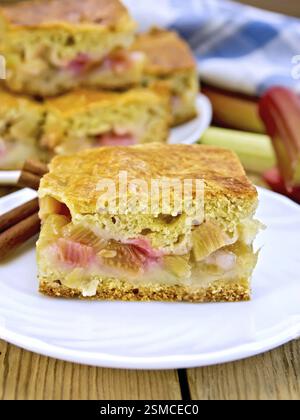 Morceaux de gâteau sucré avec de la rhubarbe dans une assiette, serviette, tiges de rhubarbe sur un fond de planches en bois Banque D'Images