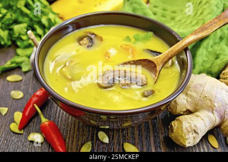 À soupe de potiron purée aux crevettes et aux champignons, une cuillère dans une tasse marron, serviette, persil, piment rouge gousses, graines de citrouille, de gingembre et de bois foncé Banque D'Images