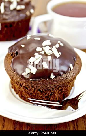 Cupcake chocolat, fourchette sur une assiette blanche, petit gâteau sur une serviette, le thé dans la tasse sur l'arrière-plan de planches en bois Banque D'Images