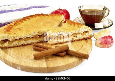 Tarte aux pommes avec des bâtonnets de cannelle sur une planche ronde en bois, une pomme entière, une serviette, du thé dans la tasse brune avec deux morceaux de sucre, deux tranches d'isol de pomme Banque D'Images