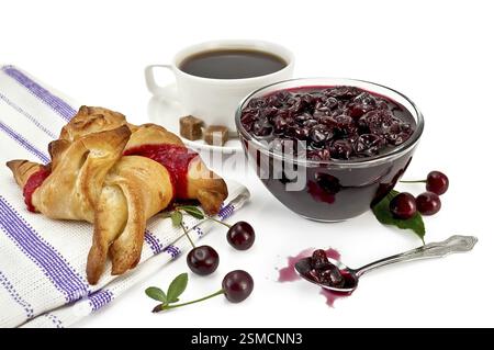 Confiture de cerises dans un bol en verre, cuillère, cerises avec des feuilles vertes, tasse en porcelaine blanche avec du café, deux morceaux de sucre, chignon avec confiture sur une serviette isolée Banque D'Images