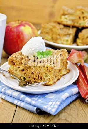 Un morceau de gâteau sucré avec de la rhubarbe, des pommes et une boule de glace, menthe, bleu, serviette tasse sur l'arrière-plan de planches en bois Banque D'Images