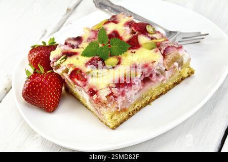 Part de tarte aux fraises, rhubarbe et à la crème, fourche, fraise, menthe en plaque blanche sur un fond en bois Banque D'Images