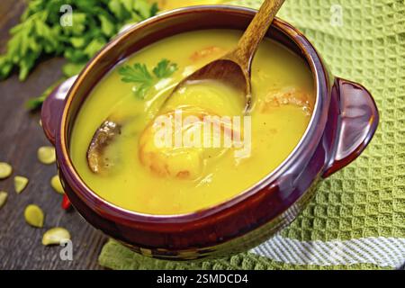 Soupe-purée citrouille avec des crevettes et des champignons, cuillère dans un bol en argile sur une serviette, persil, gousses de poivron rouge chaud, graines de citrouille sur le fond de w foncé Banque D'Images