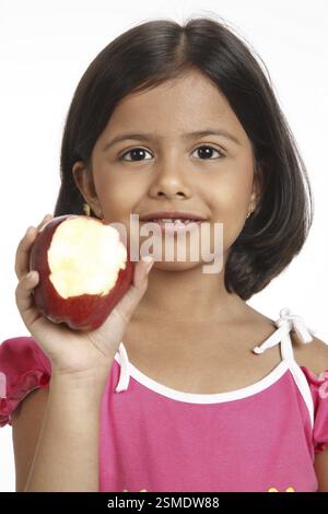 Fillette de huit ans montrant à moitié mangé par apple tenant dans sa main droite près de son visage MR# 703U Banque D'Images