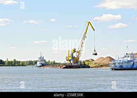 Chargement de sable à l'aide d'une grue sur une barge sur le fond d'eau et de ciel de sable jaune. River White, Russie, Europe Banque D'Images