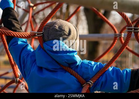Vue d'un garçon dans une veste bleue sur les cordes à l'aire de jeux Banque D'Images